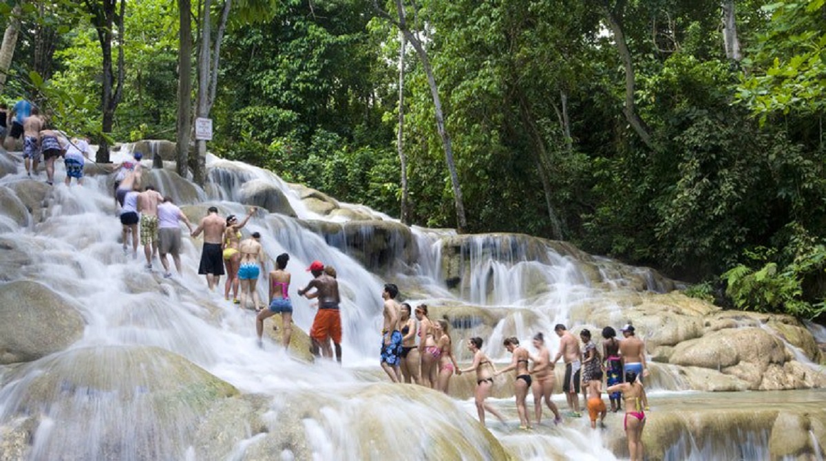 Group of people climbing up the terraced cascades of Dunn's River Falls in Jamaica, with rushing water and lush green foliage surrounding them