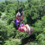 ourist ziplining in Jamaica, soaring through the air above lush rainforest and the sparkling Caribbean Sea